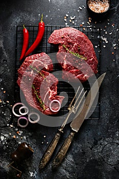 Two Raw beef steak with spices, onions and chili on dark slate or concrete background.