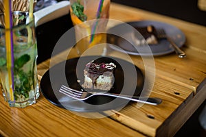 Two raw cakes with chocolate on black and grey plates with forks standing on wooden table