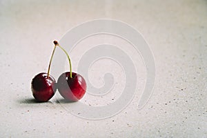 Two  raw cherries on a marble table base with an empty copy space for text, selective focus and toned image