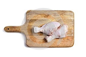 Two raw chicken legs with skin lying on a wooden cutting board. Fresh uncooked meat of poultry isolated on white background. Top