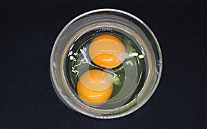 Two Raw Eggs In A Glass Bowl On Black Surface Top View