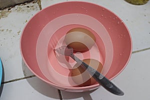 Two raw eggs are in a pink bowl