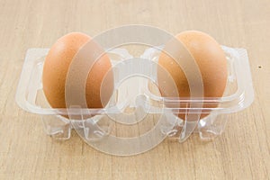 Two raw eggs in plastic box on wood board