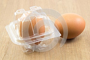 Two raw eggs in plastic box on wood board