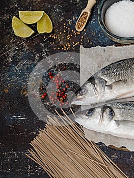 Two raw fish sea bass and other ingredients on dark vintage background