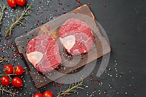 Two raw fresh marbled meat steak on dark background, cherry tomatoes and spices.