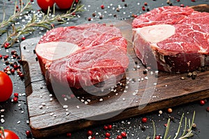 Two raw fresh marbled meat steak on dark background, cherry tomatoes and spices.