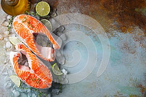 Two raw fresh salmon or trout steaks on ice, rich in omega-3 oil, with lime, thyme and olive oil on a blue rusty background.