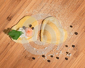 Two raw handmade ravioli ,open and closed,in the shape of heart,covered with flour and placed on wooden table