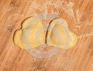 Two raw handmade ravioli in the shape of heart,covered with flour and placed on the wooden table.