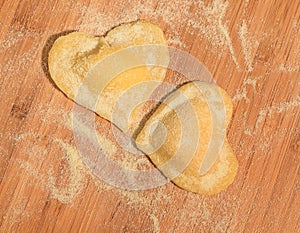 Two raw handmade ravioli in the shape of heart,covered with flour and placed on the wooden table.