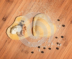 Two raw homemade ravioli,open and closed,in the shape of heart,covered with flour and placed on wooden table.