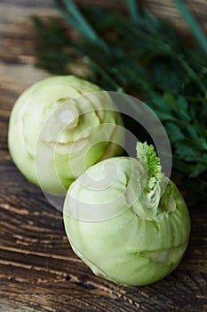 Two raw kohlrabies with some herbs dill, parsley and chives on a rustic wooden table.