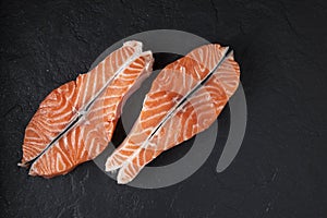 Two raw salmon steaks on a black textured background. Closeup