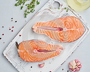Two raw salmon steaks, fish fillet,  large sliced portions  on chopping board on a white table. Top view. Food background