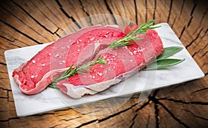 Raw steak meat on white dish with tree trunk background