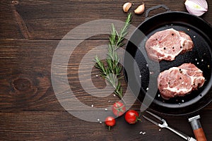 Two raw steaks on frying pan on rustic wooden background. Pieces of meat ready for cooking.