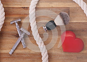 Two razors, brush, heart and rope on wooden background
