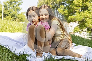 Two Real Little Girls, Sisters Hugging On Grass in Meadow At Sunny Day. Caucasian Asian