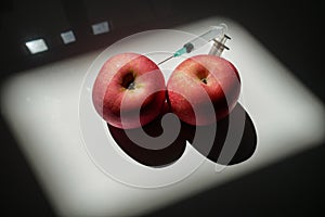 Two red apples that can symbolize two full breasts or two muscular testicles in which is planted a syringe