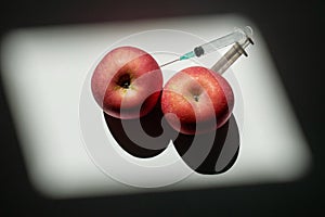 Two red apples that can symbolize two full breasts or two muscular testicles in which is planted a syringe