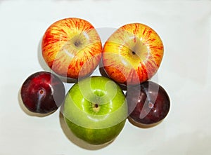 Two red apples and one green apple and two plum on white background