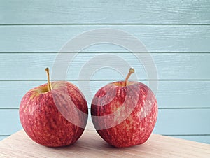 two red apples with water droplets on corner of kitchen table and blue wooden paneling wall background