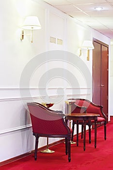 Two red armchairs with round wooden table on red carpet