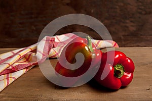 Two red bell pepper on wooden background with red kitchen towel