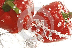 Two red bell peppers splashing in water