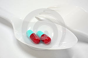 Two red and blue capsules on plastic spoon fork