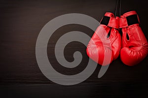 Two red boxing gloves hanging on a black background in the corner of the frame