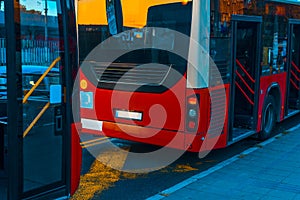 Two red bus on buses stop at city street on evening time of the day