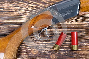 Two red cartridges on a dark wooden board, and a hunting rifle