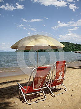 Two red chairs and one umbrella in the beach with a lear blue sky