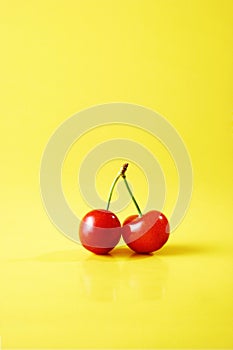 Two red cherries against yellow background