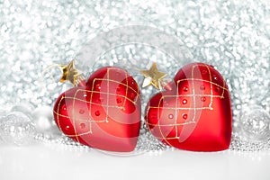 Two red Christmas tree glass balls in the shape of heart with golden stars and silver and red balls on shiny sparkling tinsel