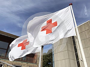 Two Red Cross flags waving in the wind against a blue sky.