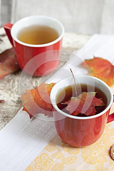 Two red cups with tea on a yellow tablecloth with autumn leaves