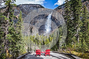 Two red deckchairs for tourists opposite waterfall.