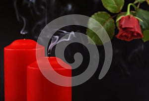 Two red extinguished candles with white smoke and withered rose flower on black