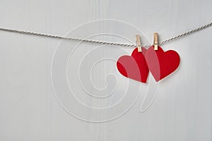 Two red felt valentine hearts hanging from a rope on white wooden background