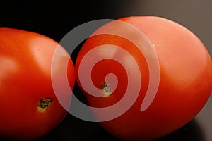 Two red fresh tomatoes. Mature. Dimmed light. On black background.