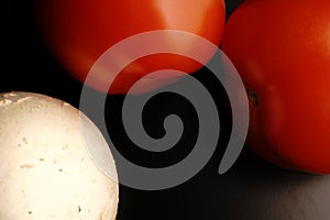 Two red fresh tomatoes. Mature. Dimmed light. On black background.