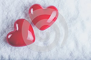 Two red glossy hearts on a frosty white snow background. Love and St. Valentine concept.