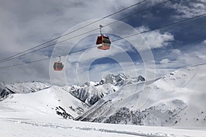 Two red gondolas on sky and cloudly background lift people in high mountains.