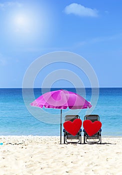 Two red heart on beach chair under pink umbrella with space on blue sea and clear sky background, summer outdoor day light
