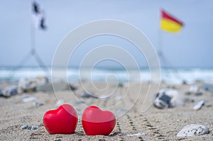 Two red hearts on the beach with surf flags in the background