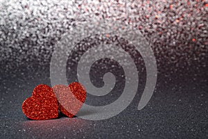 two red hearts in glitter on a silver glitter background