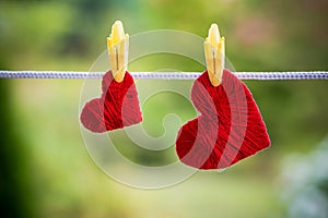 Two red hearts hanging on the rope fixed by clothespins isolated on blurred green background.Valentines Day and Happy